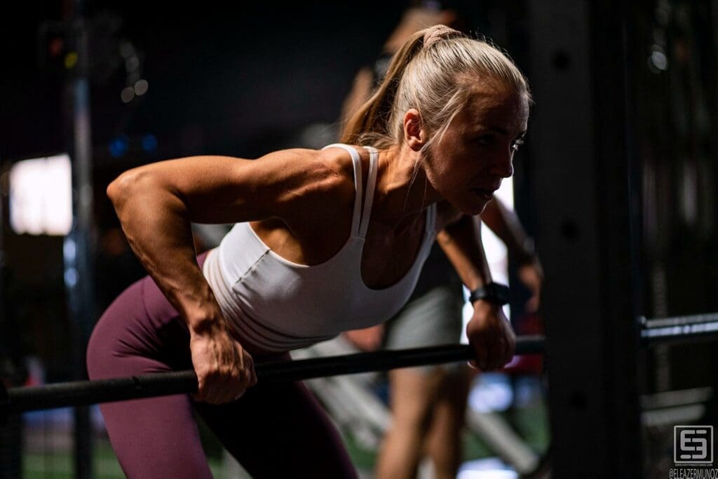 A fitness model lowers into a parallel-bar dip under directional gym lighting.