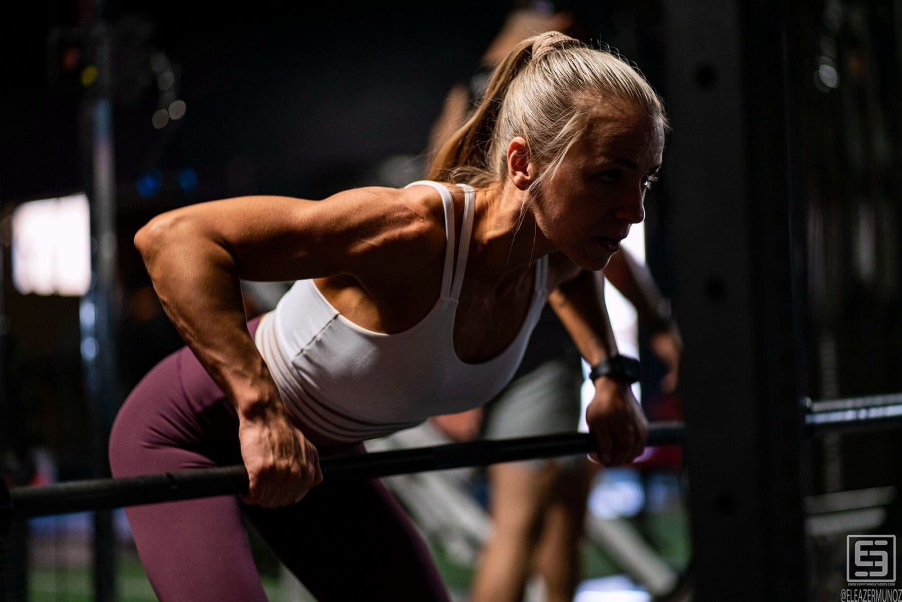 A fitness model lowers into a parallel-bar dip under directional gym lighting.