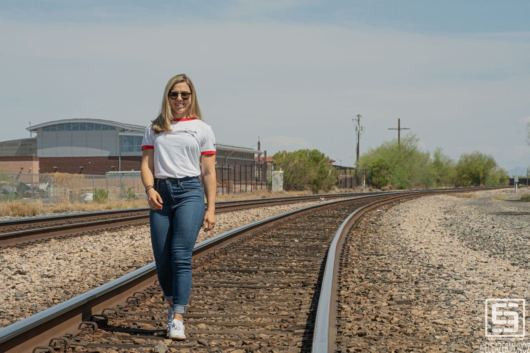 Day Muñoz walks toward the camera along curving railroad tracks in a white ringer T-shirt and jeans.