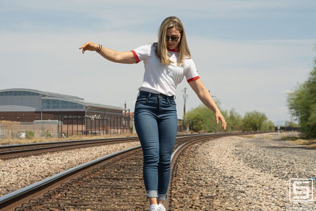 Day Muñoz extends her arms while balancing along a railroad rail in a casual white shirt and jeans.