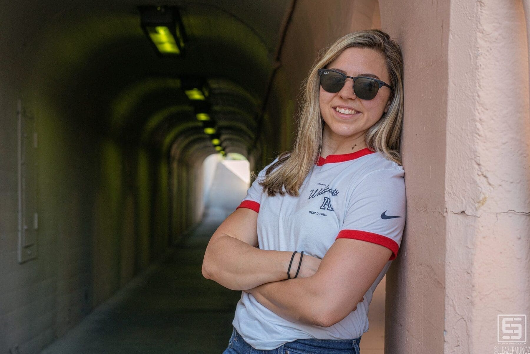 Day Muñoz stands with arms crossed in a white ringer T-shirt and sunglasses beside an arched passage.