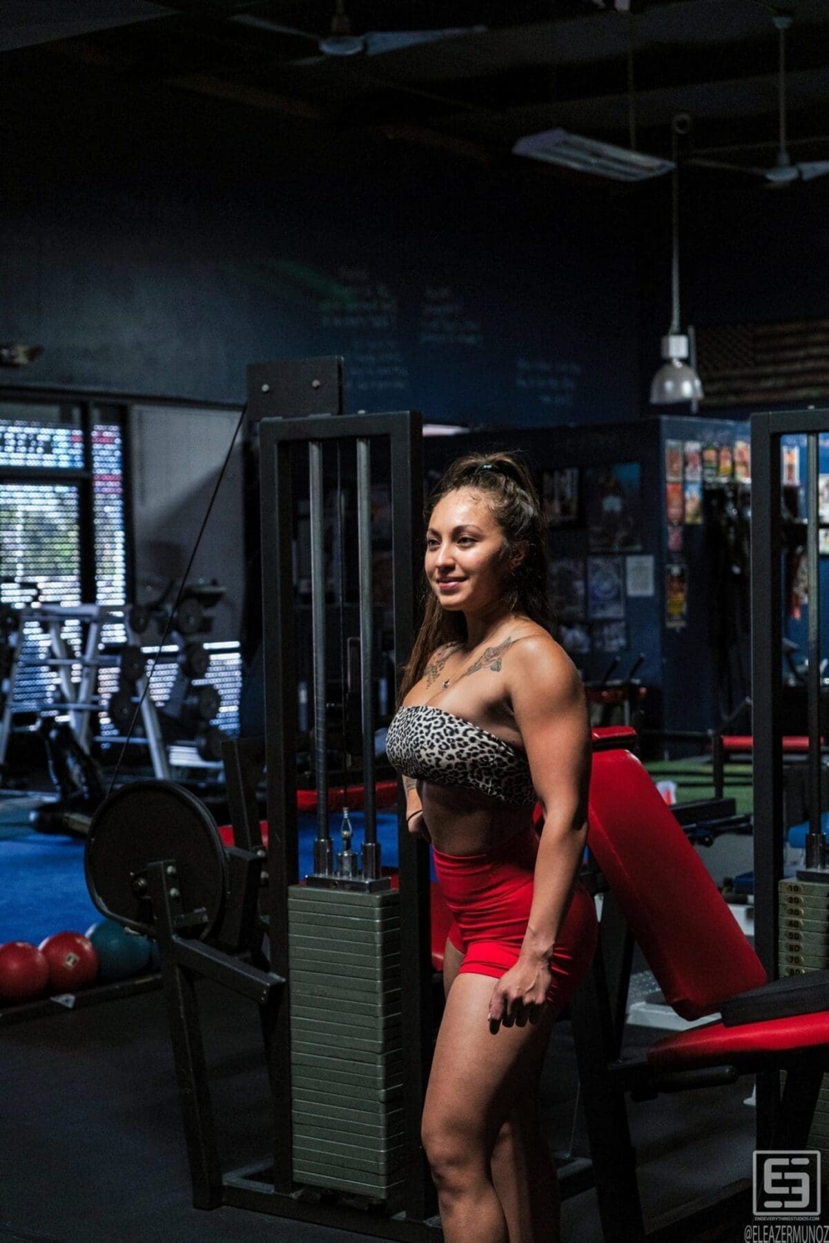Danni stands in profile beside a weight machine in a leopard-print top and red shorts.