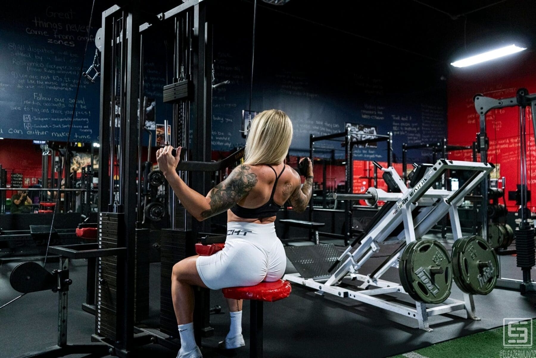 Rear view of Cami Bee seated at a cable station with her arms raised.