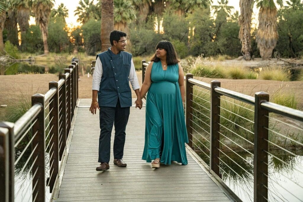 Aditi and her partner walk hand in hand toward the camera along the bridge above the water.