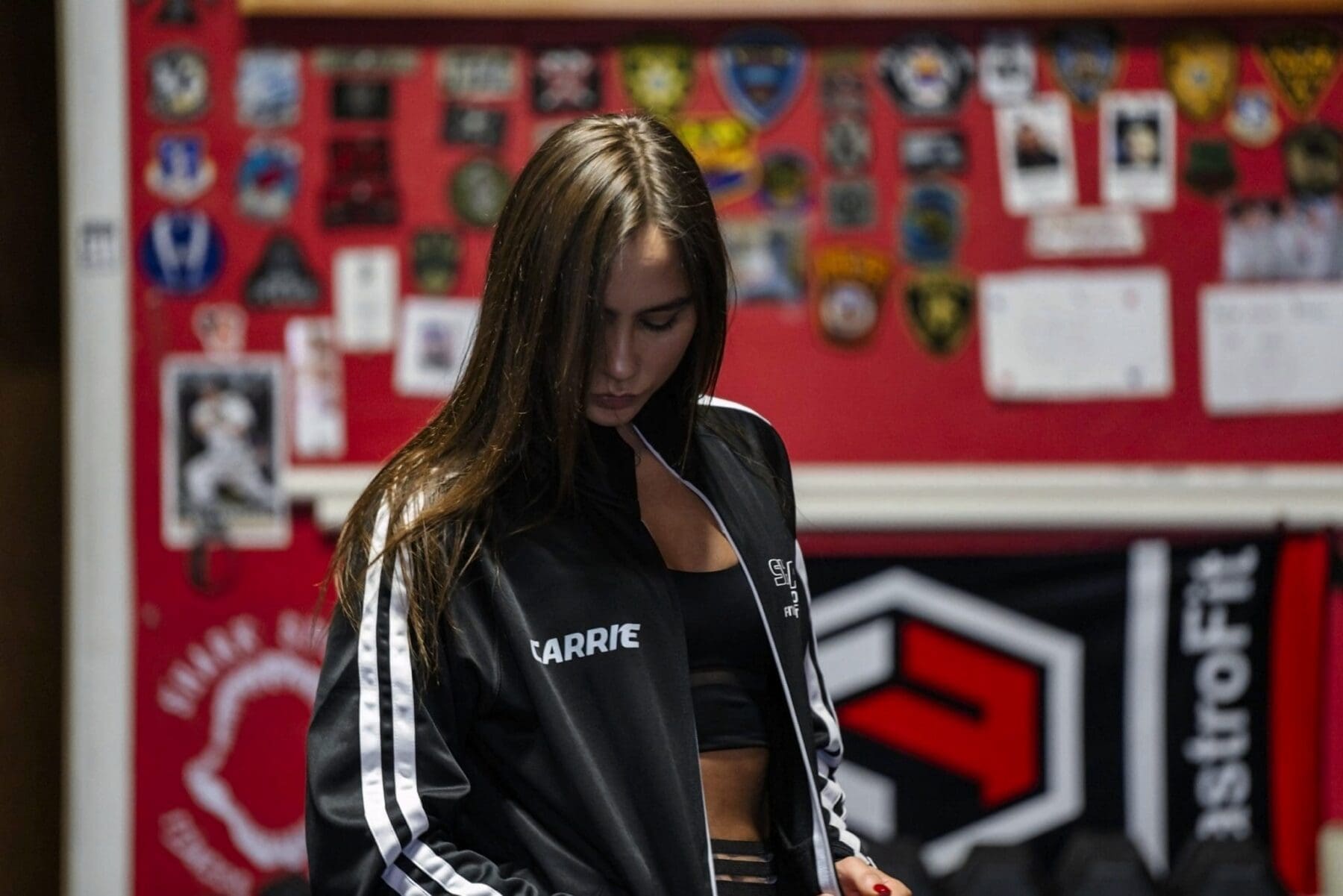 Carrie faces the camera in a black Shark Sports competition team jacket inside the gym.