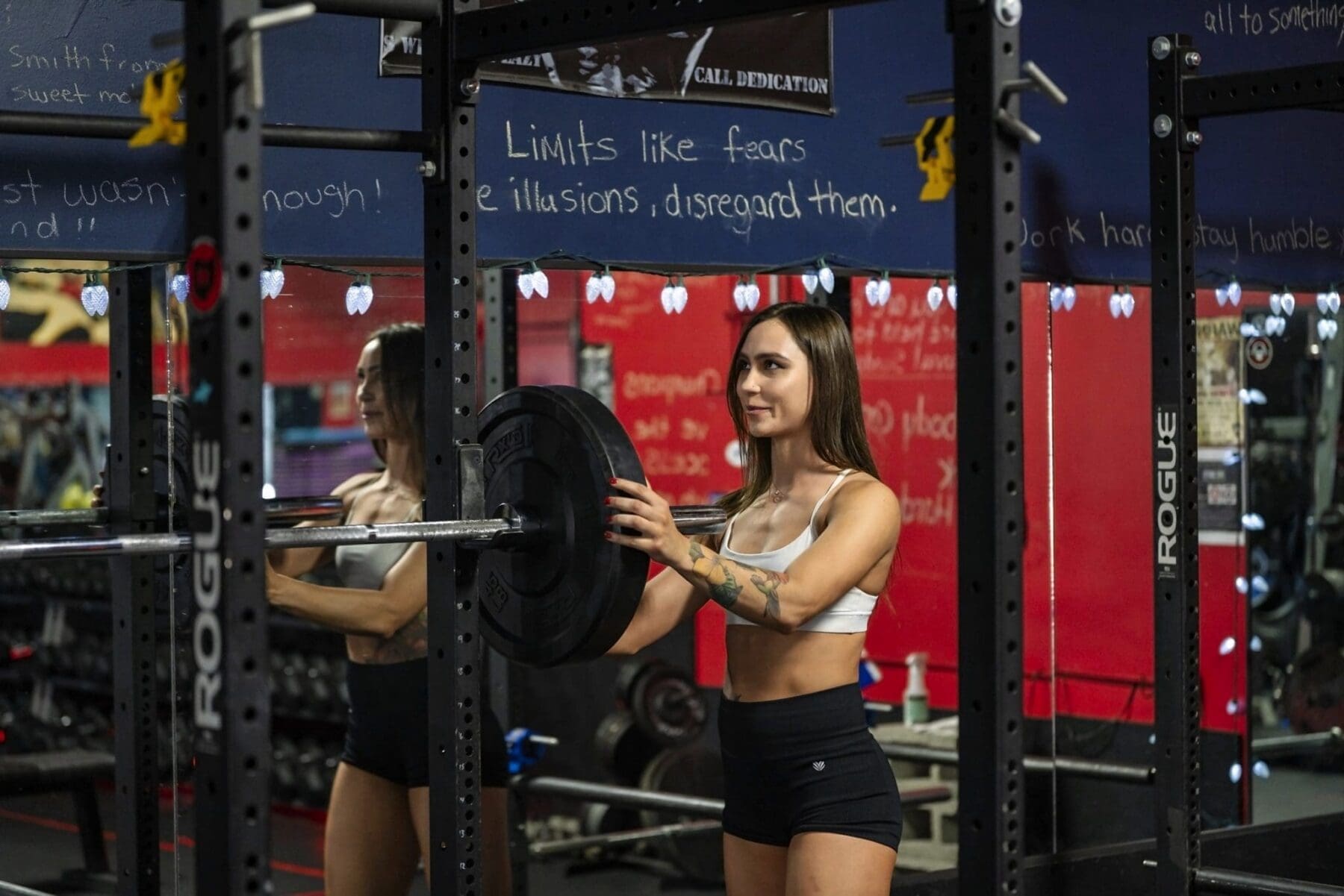 Carrie holds a weight plate beside a barbell rack in the gym.