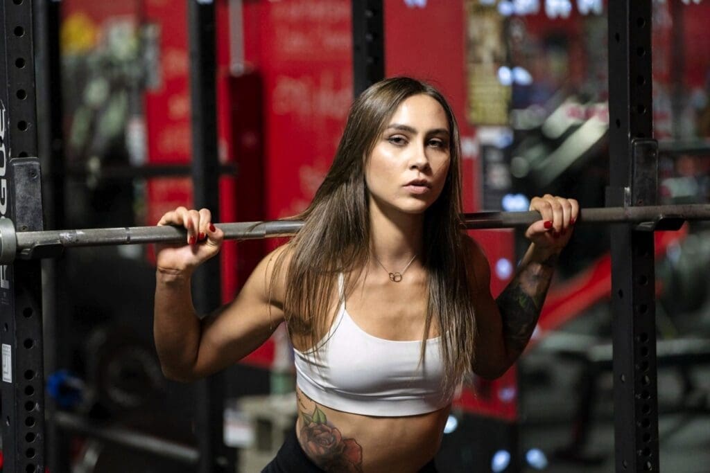 Carrie poses beside a barbell inside a power rack at Shark Sports Fitness.