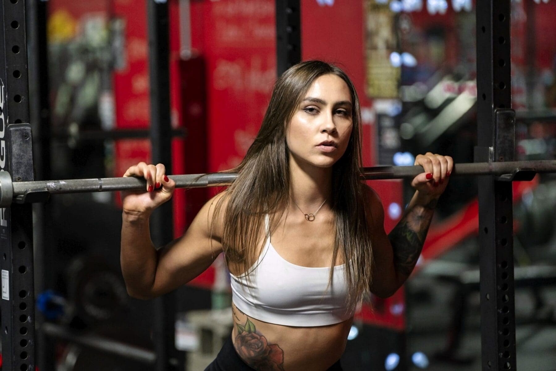 Carrie poses beside a barbell inside a power rack at Shark Sports Fitness.
