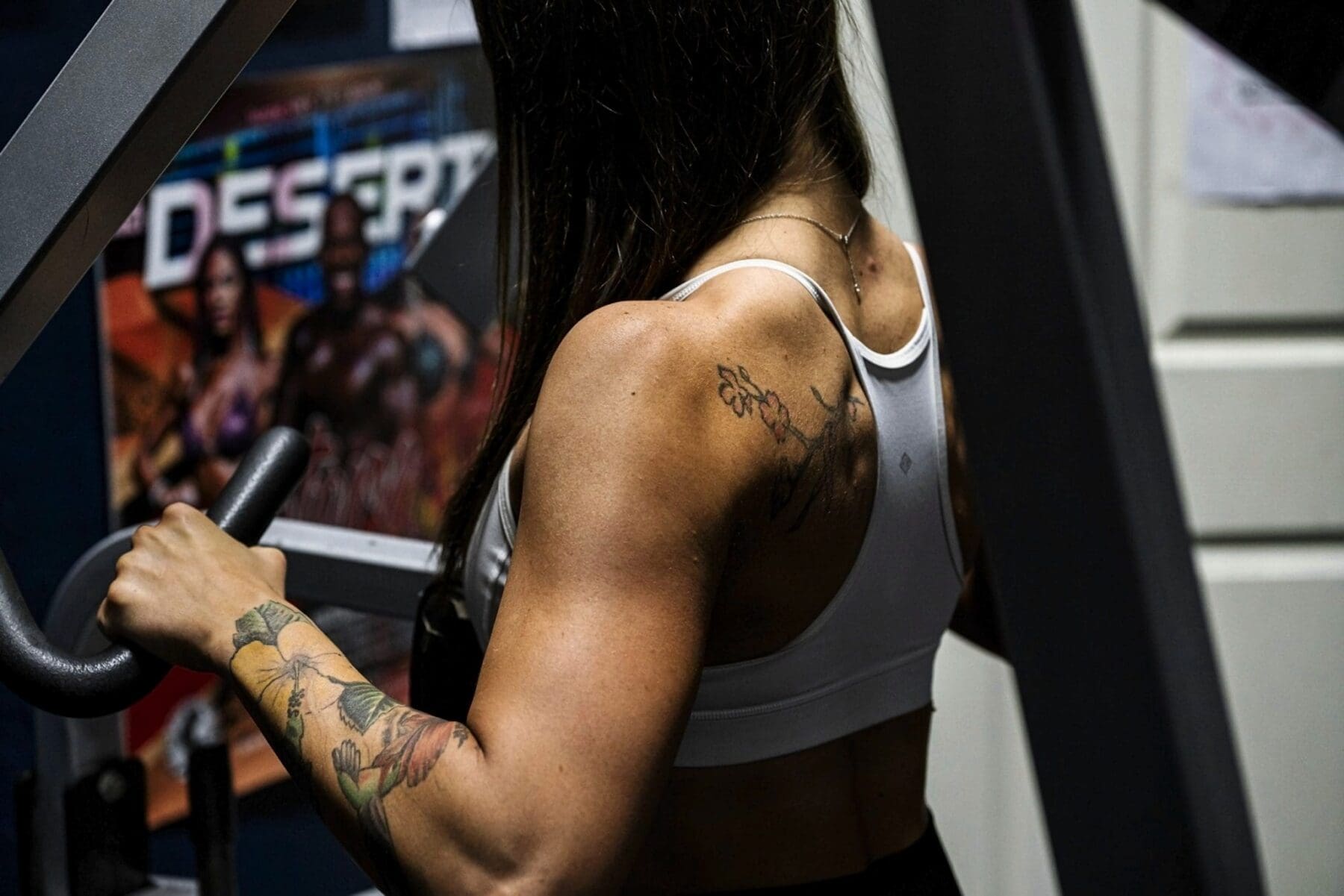 Close rear view of Carrie using a resistance machine with back definition visible.