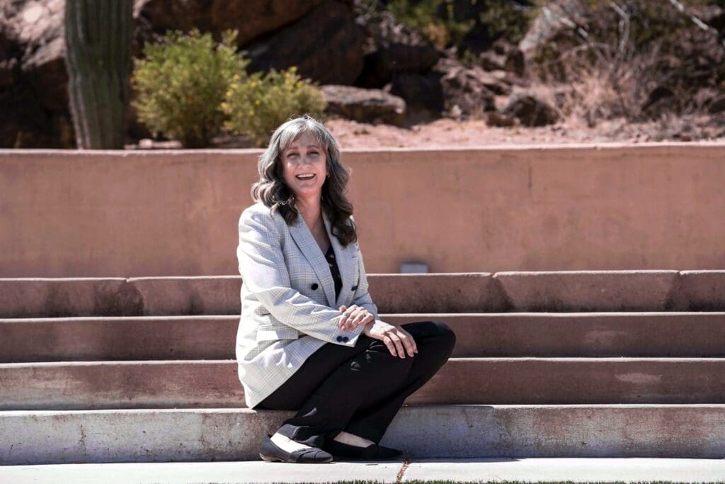 Cathy Byroad sits on broad outdoor steps in a light plaid blazer.