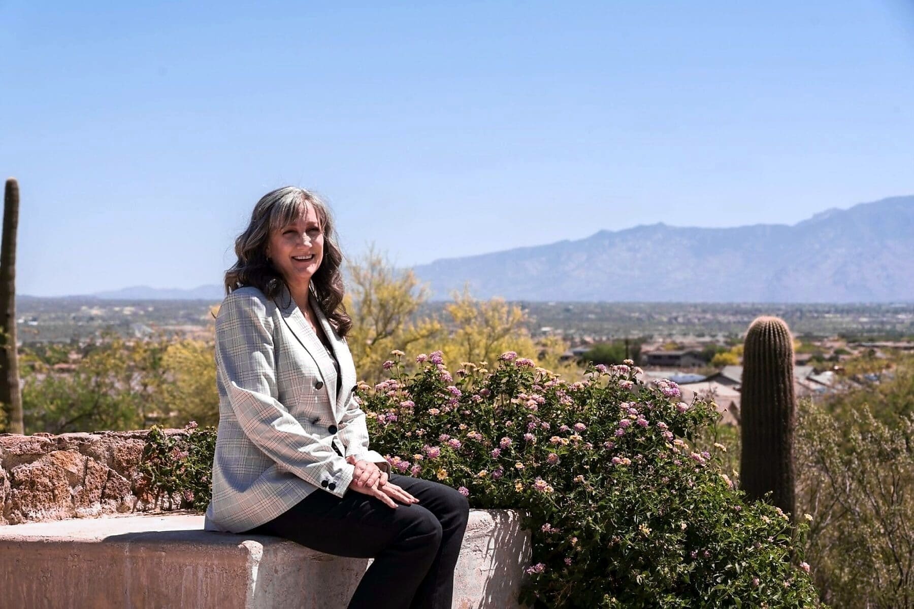 Cathy Byroad smiles while seated above a desert valley with distant mountains.