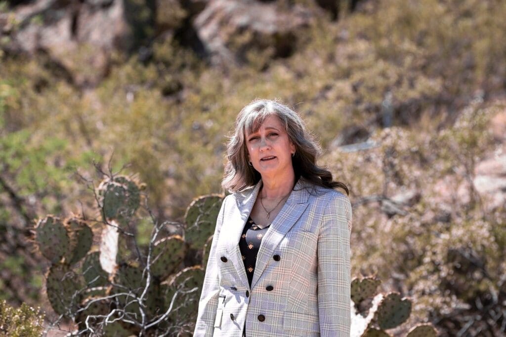 Cathy Byroad smiles in a light plaid blazer with prickly pear cactus softly behind her.