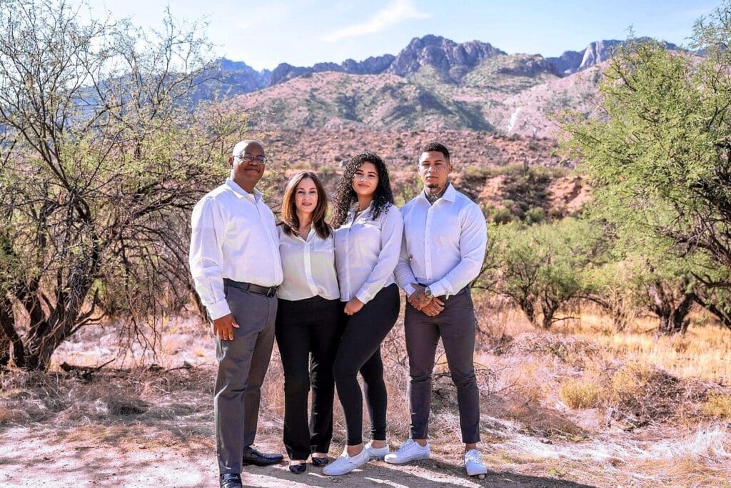 Four family members pose in coordinated white shirts against a broad mountain landscape.