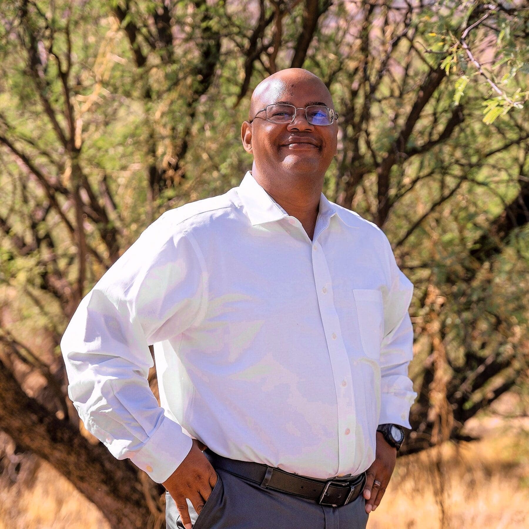 An older man in glasses and a white shirt smiles in a close desert portrait.