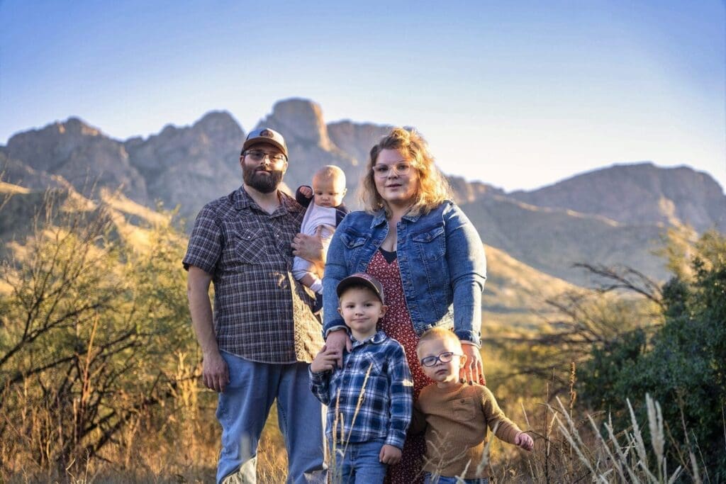 Two adults and three children stand together with desert plants and a mountain ridge behind them.