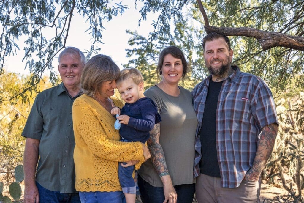 Five adults and a young child pose closely together beneath desert trees.