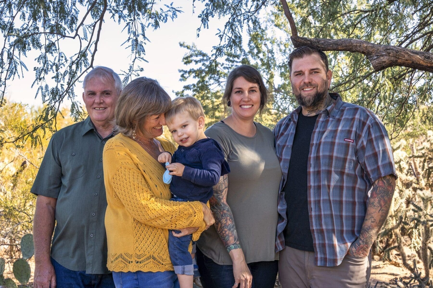 Five adults and a young child pose closely together beneath desert trees.
