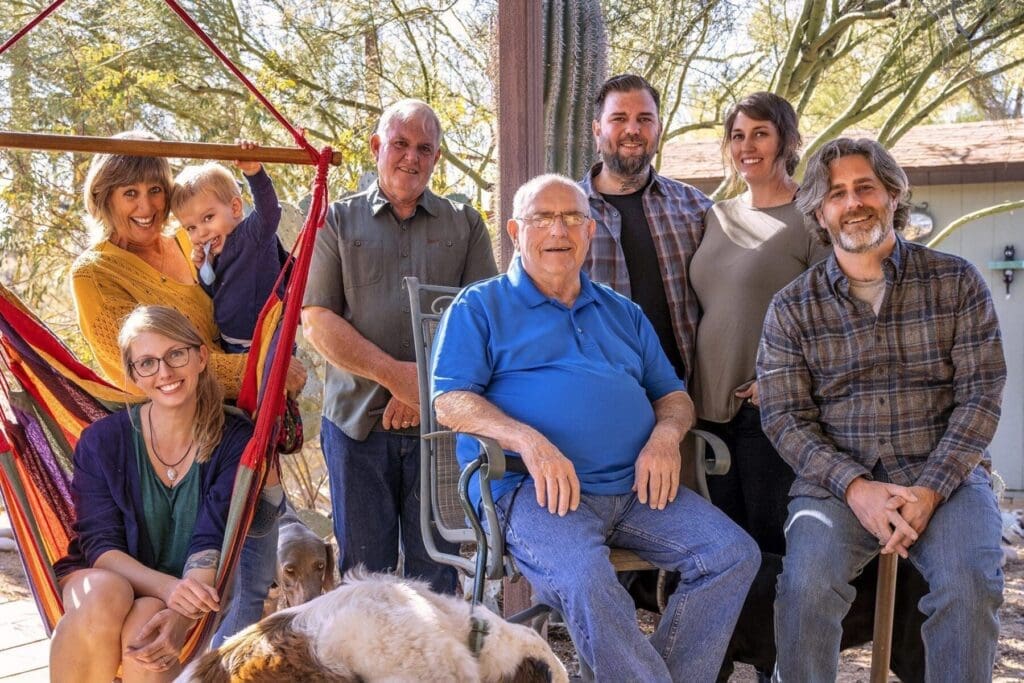 A large group poses in two rows beside a hammock with dogs at their feet.