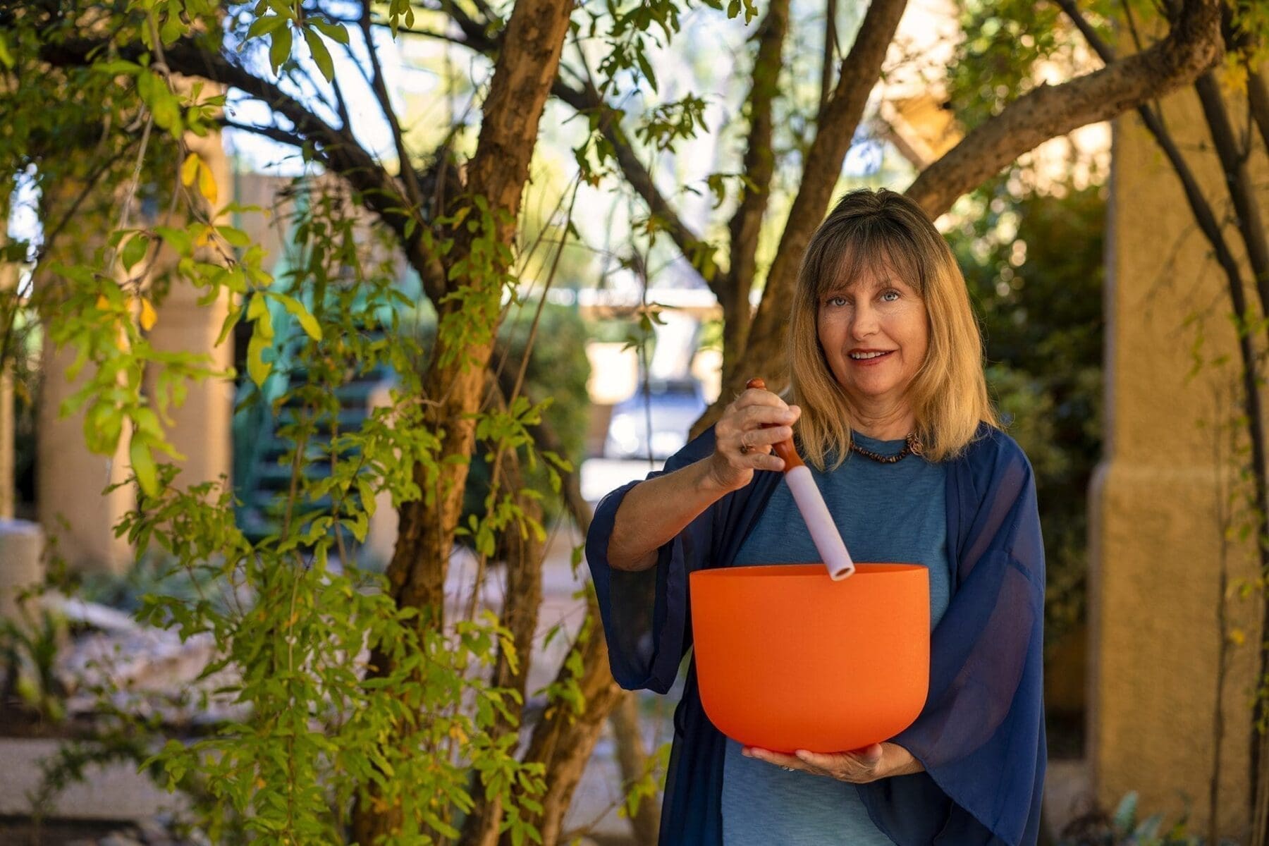 Kat Styrcula smiles outdoors while holding an orange crystal sound bowl and mallet.