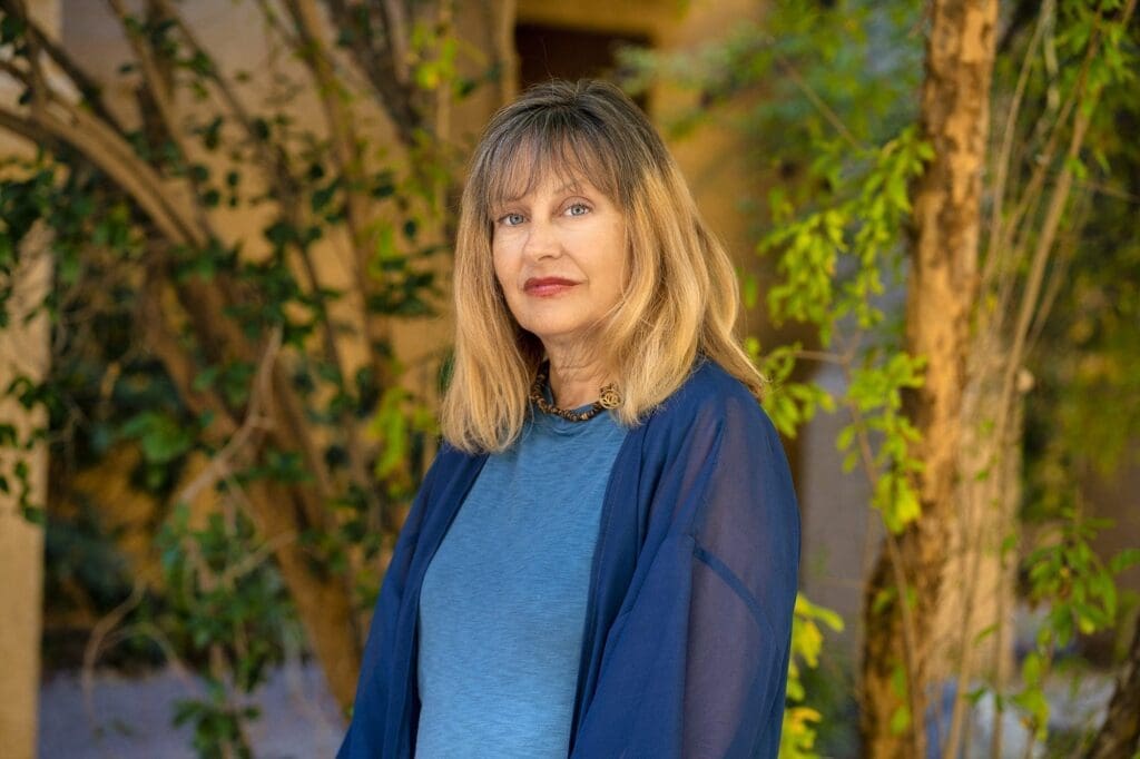 A close outdoor portrait of Kat Styrcula framed by courtyard greenery.