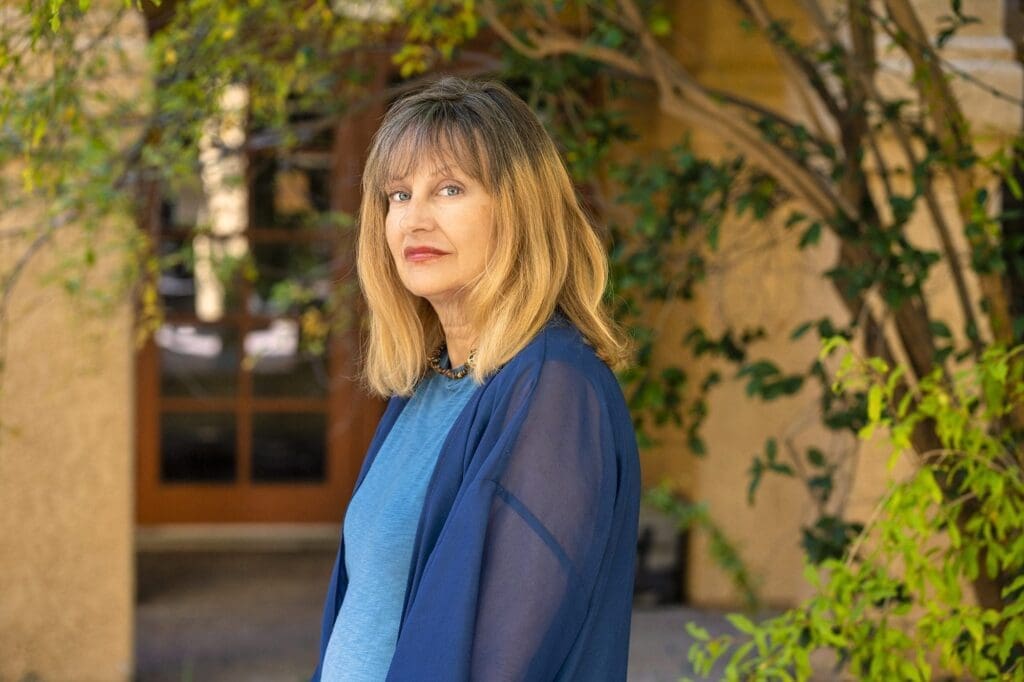 A three-quarter outdoor portrait of Kat Styrcula in a shaded courtyard setting.