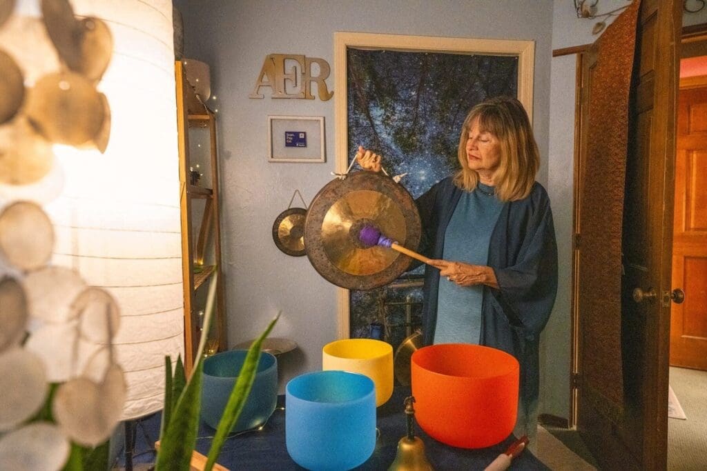 Kat Styrcula strikes a suspended gong inside her sound-therapy instrument room.