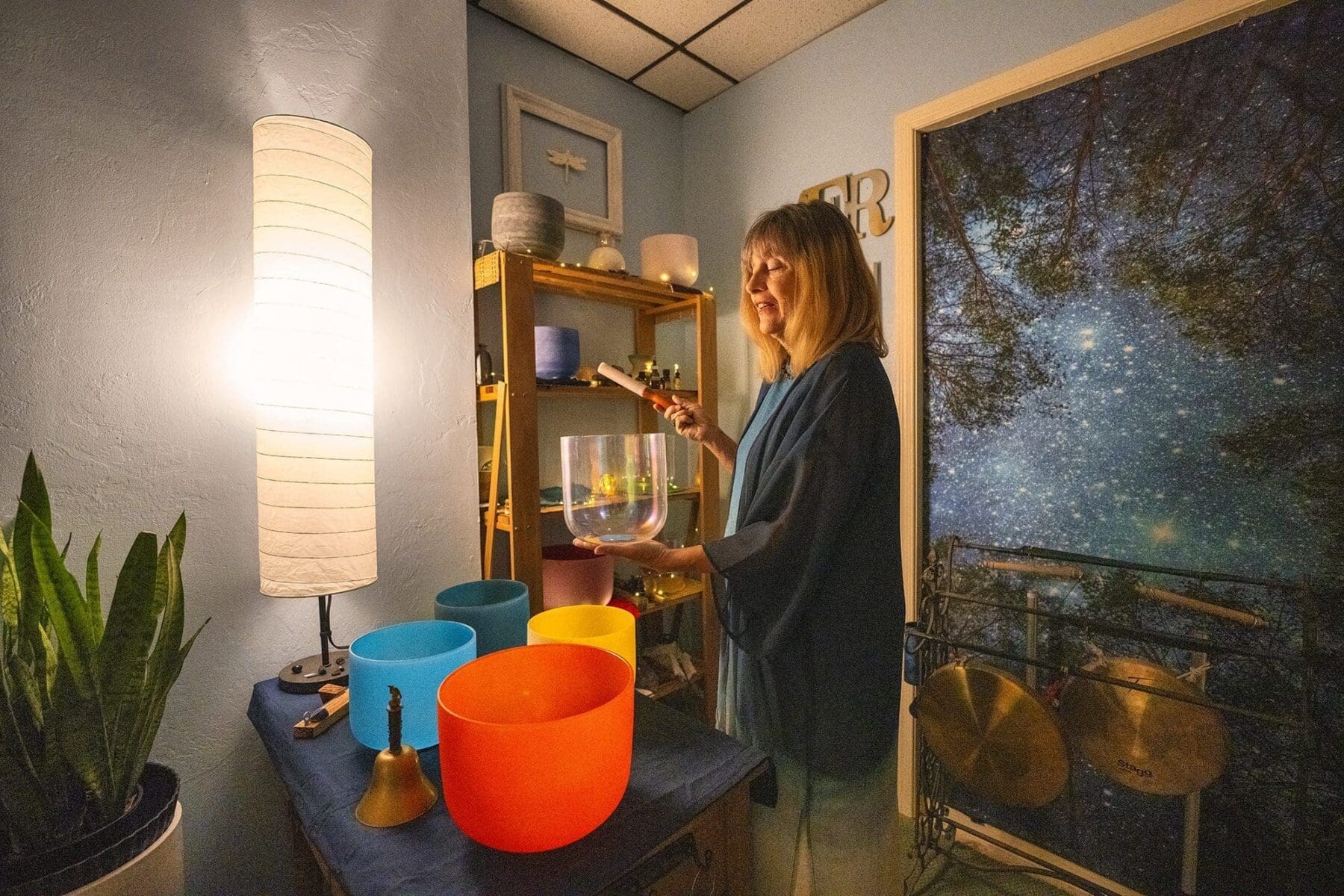 Kat Styrcula holds a translucent bowl surrounded by crystal bowls and metal instruments.
