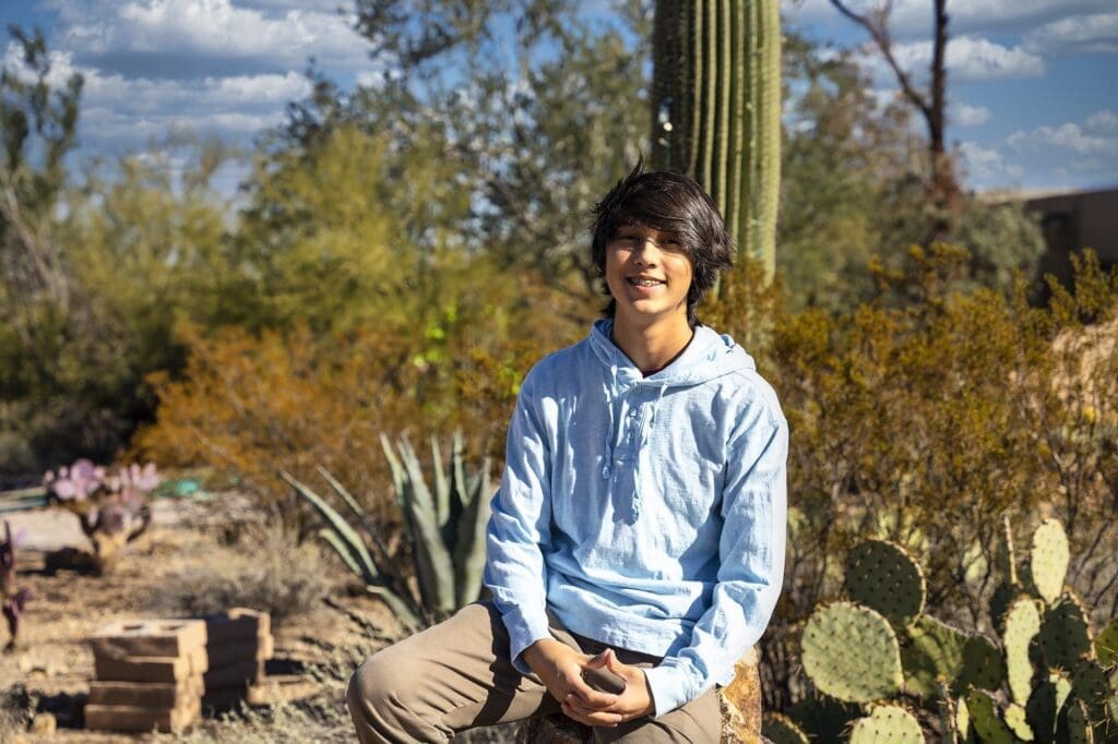 A young Simpkins family member sits on a rock in a light blue hoodie among desert cactus.