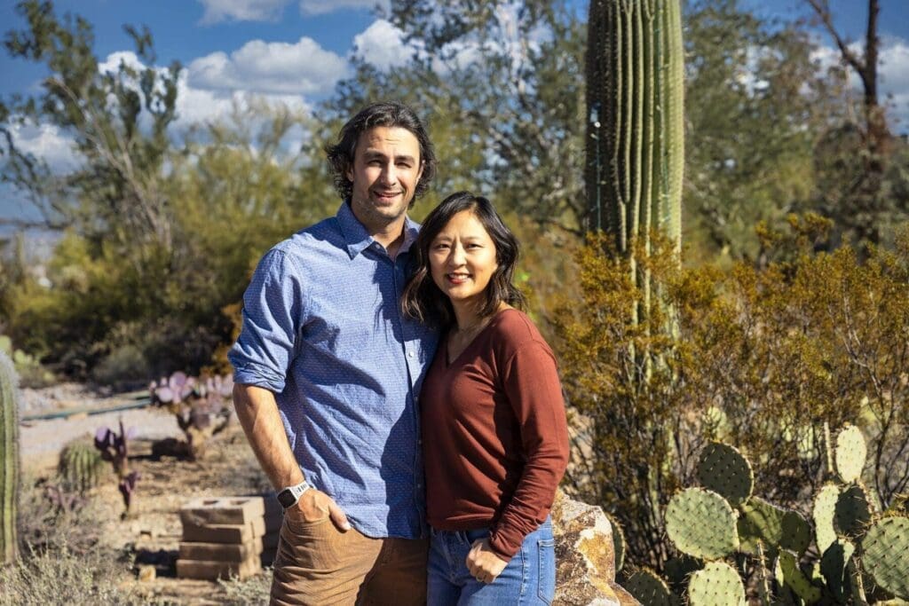 Two adult members of the Simpkins family stand closely together in front of desert cactus.
