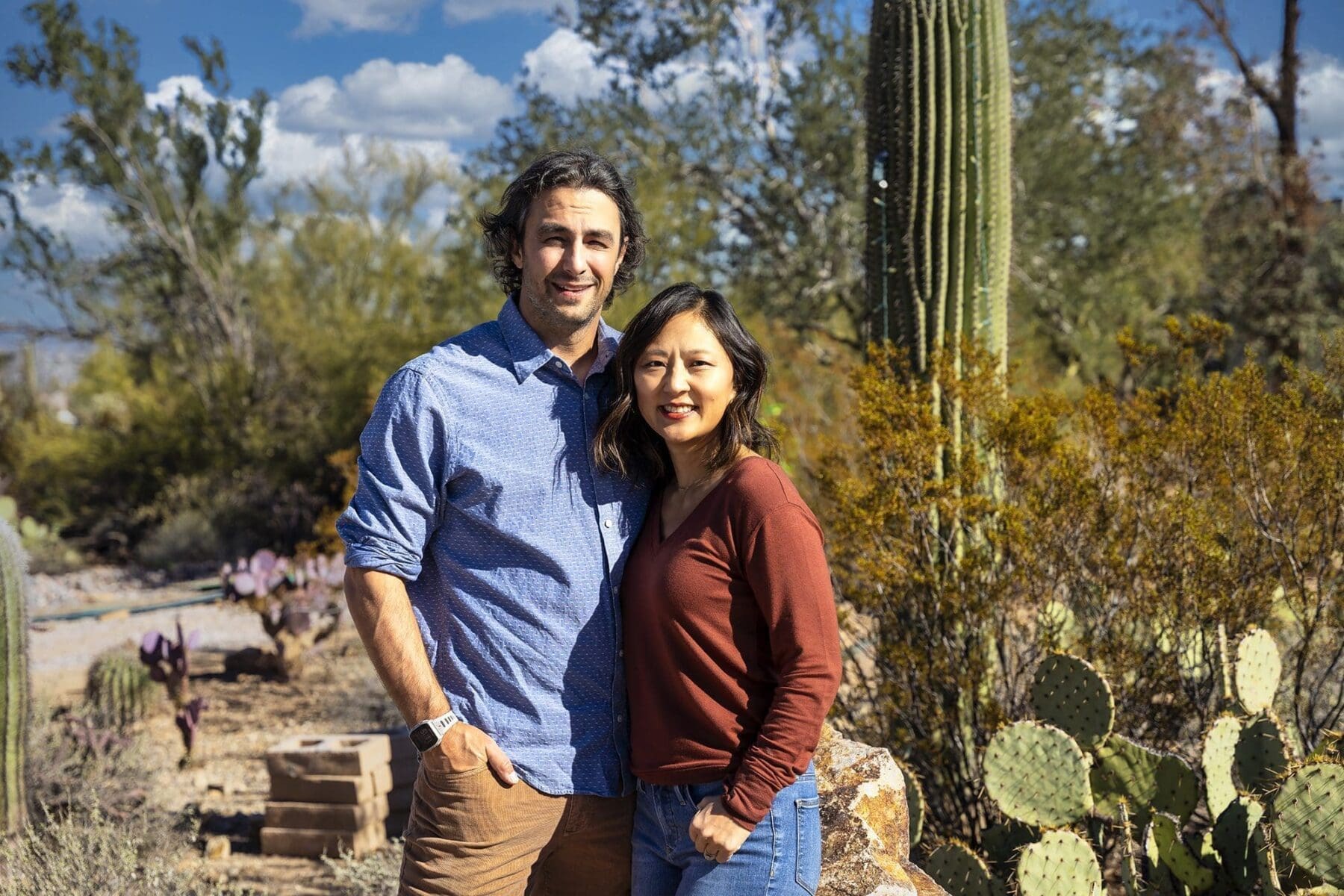 Two adult members of the Simpkins family stand closely together in front of desert cactus.