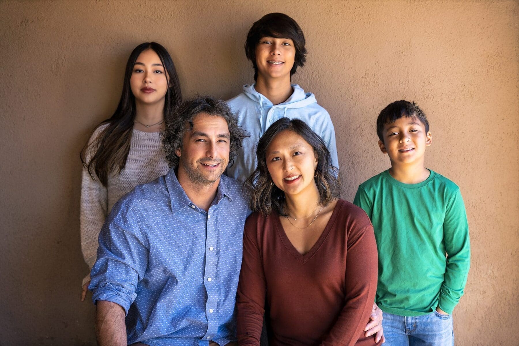 Five members of the Simpkins family gather closely against a warm adobe-colored wall.