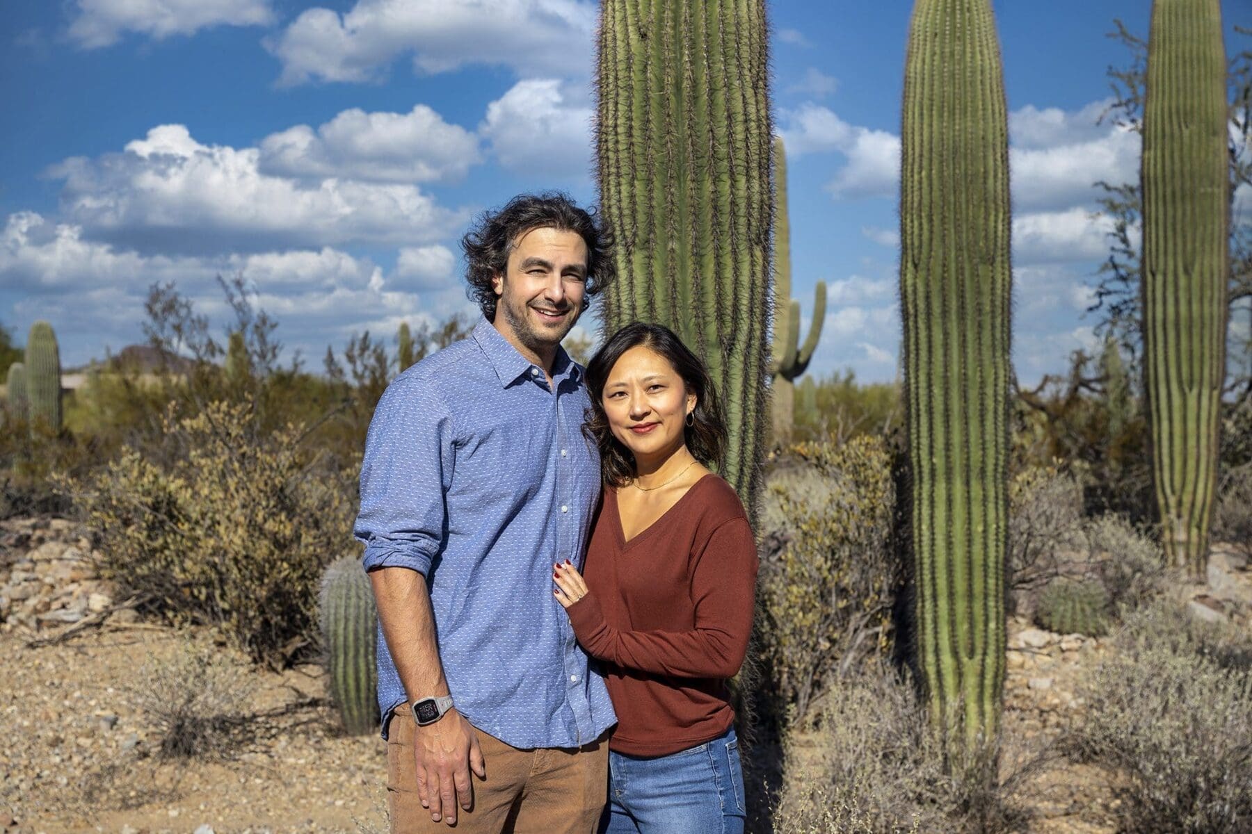 Two adult Simpkins family members stand closely together with tall saguaros behind them.