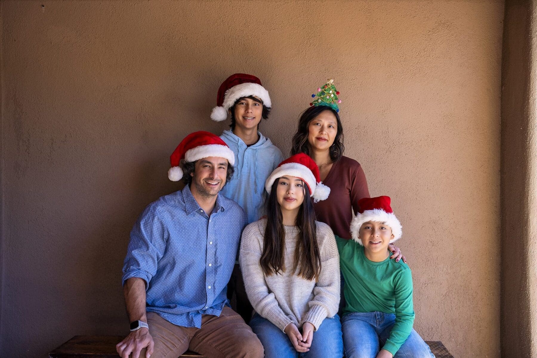 Five Simpkins family members gather against an adobe-colored wall wearing Santa and holiday hats.
