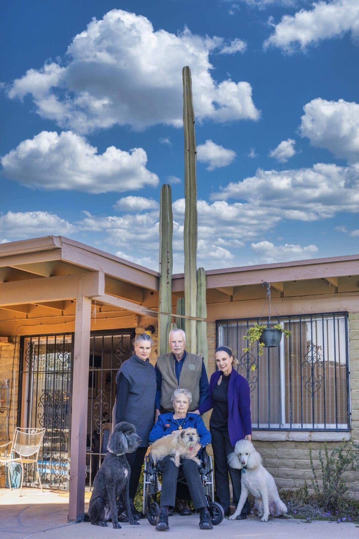 The Slack family stands with their dogs beneath a tall saguaro and bright desert sky.