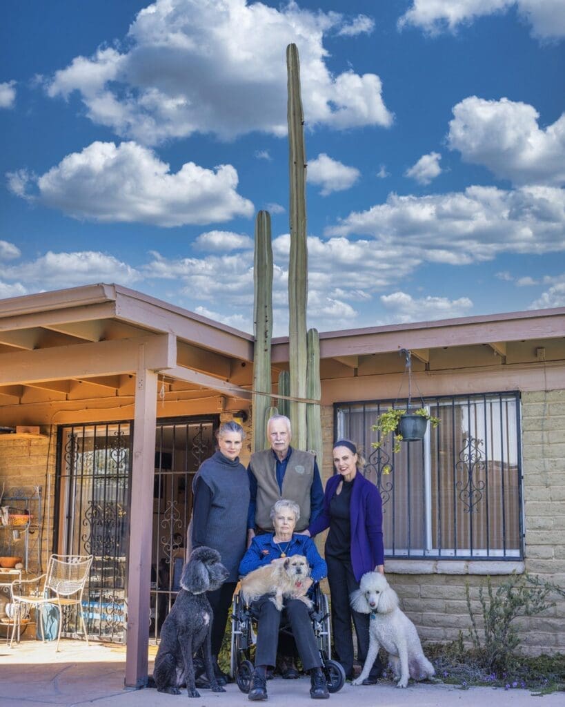 The Slack family poses with three dogs beneath a tall saguaro outside the family home.