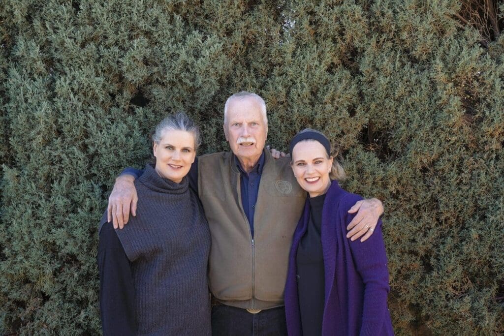Three Slack family members stand together before greenery during the Mother’s Day gift session.