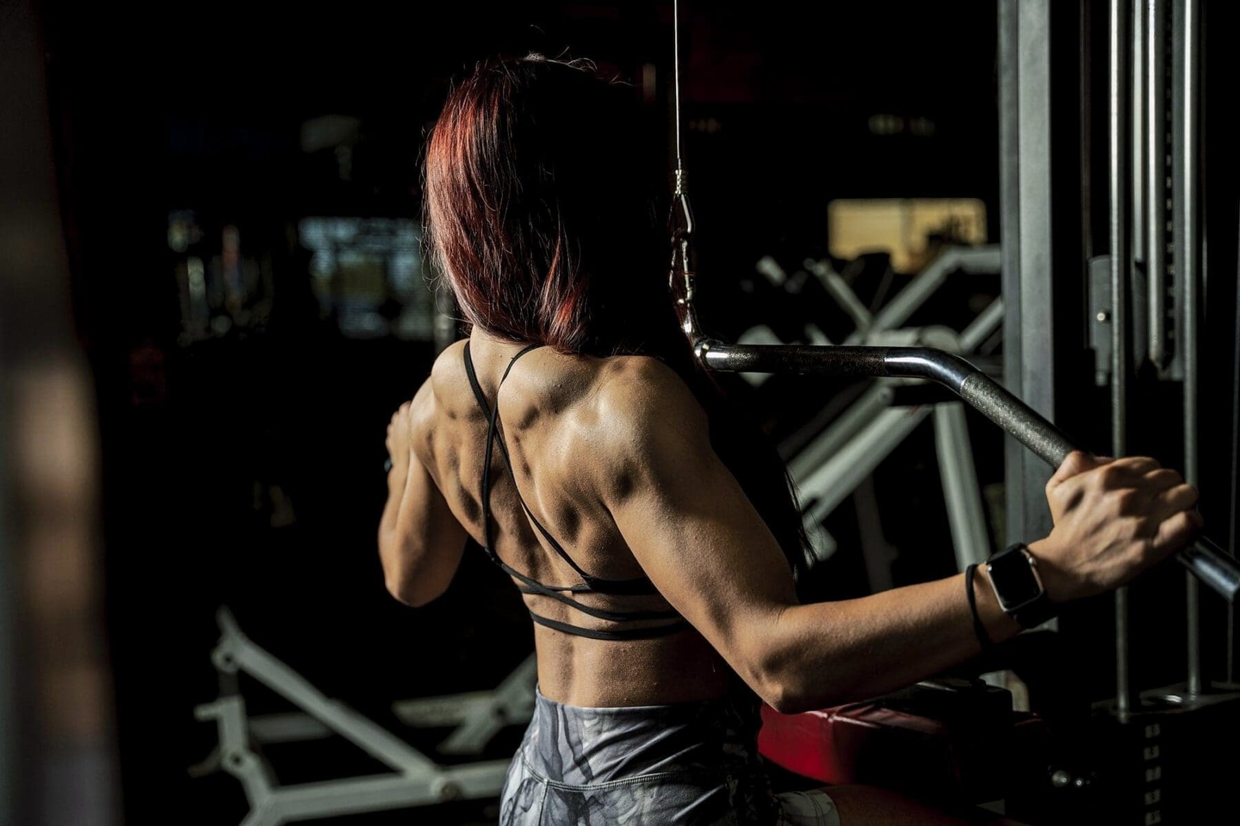 Hard side light defines Clarissa's back as she works at a cable pulldown station.