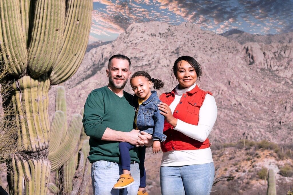 Three family members pose together beside a tall saguaro with mountains behind them.