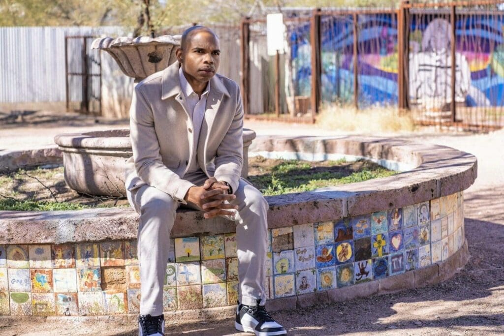 Aaron Owens sits forward with hands clasped on the edge of a mosaic fountain.