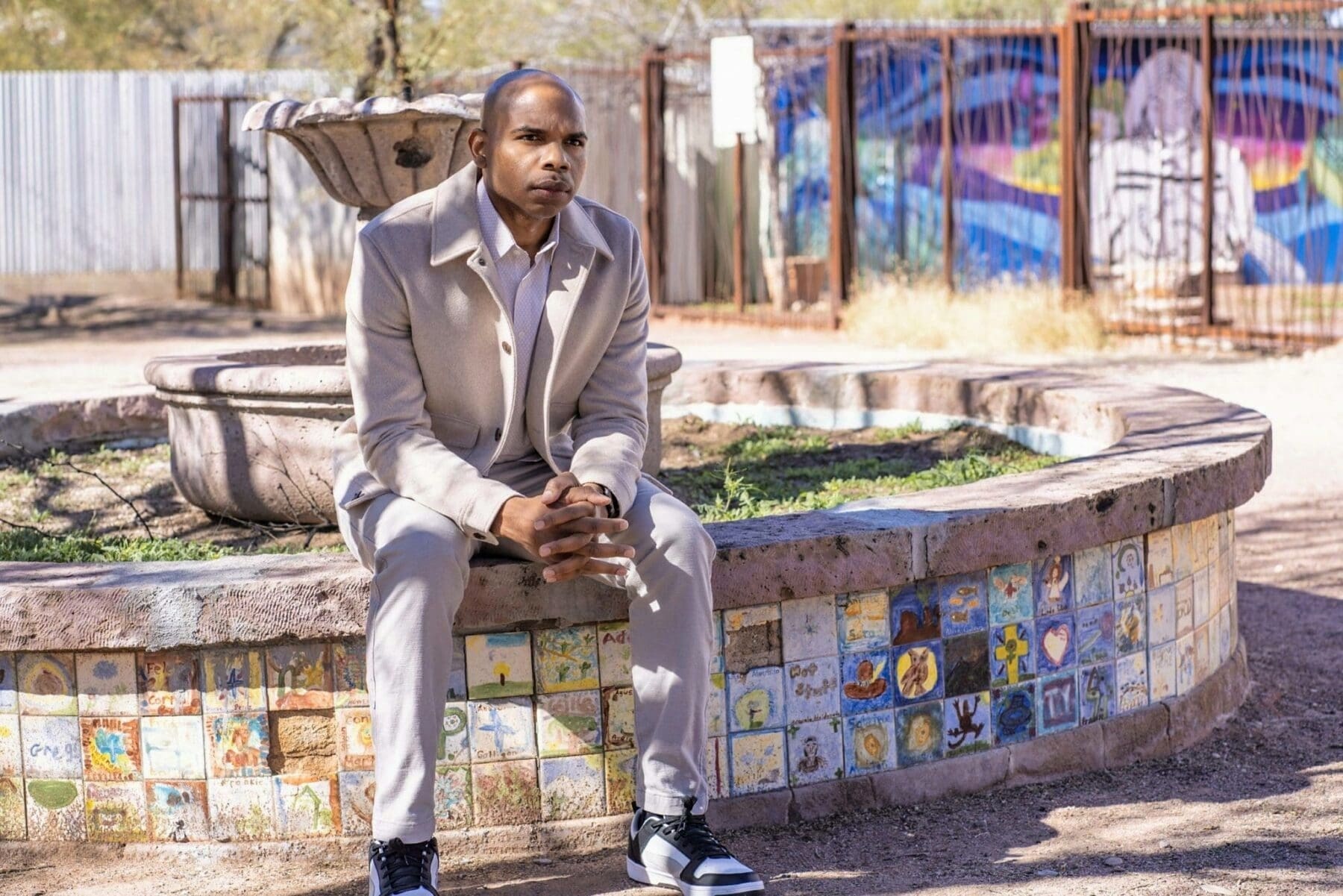 Aaron Owens sits forward with hands clasped on the edge of a mosaic fountain.