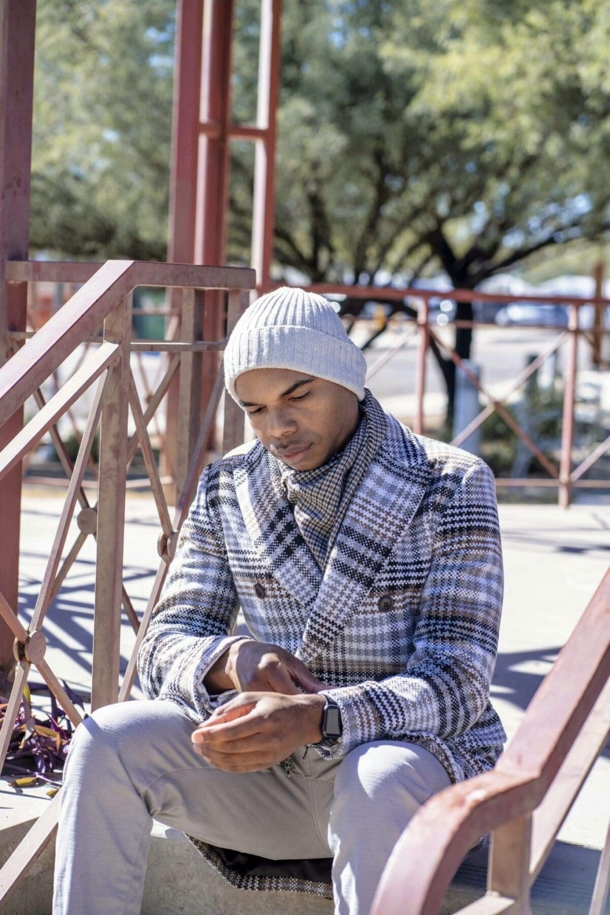 Aaron Owens sits beside a red pavilion railing in a plaid coat, scarf, and knit cap.