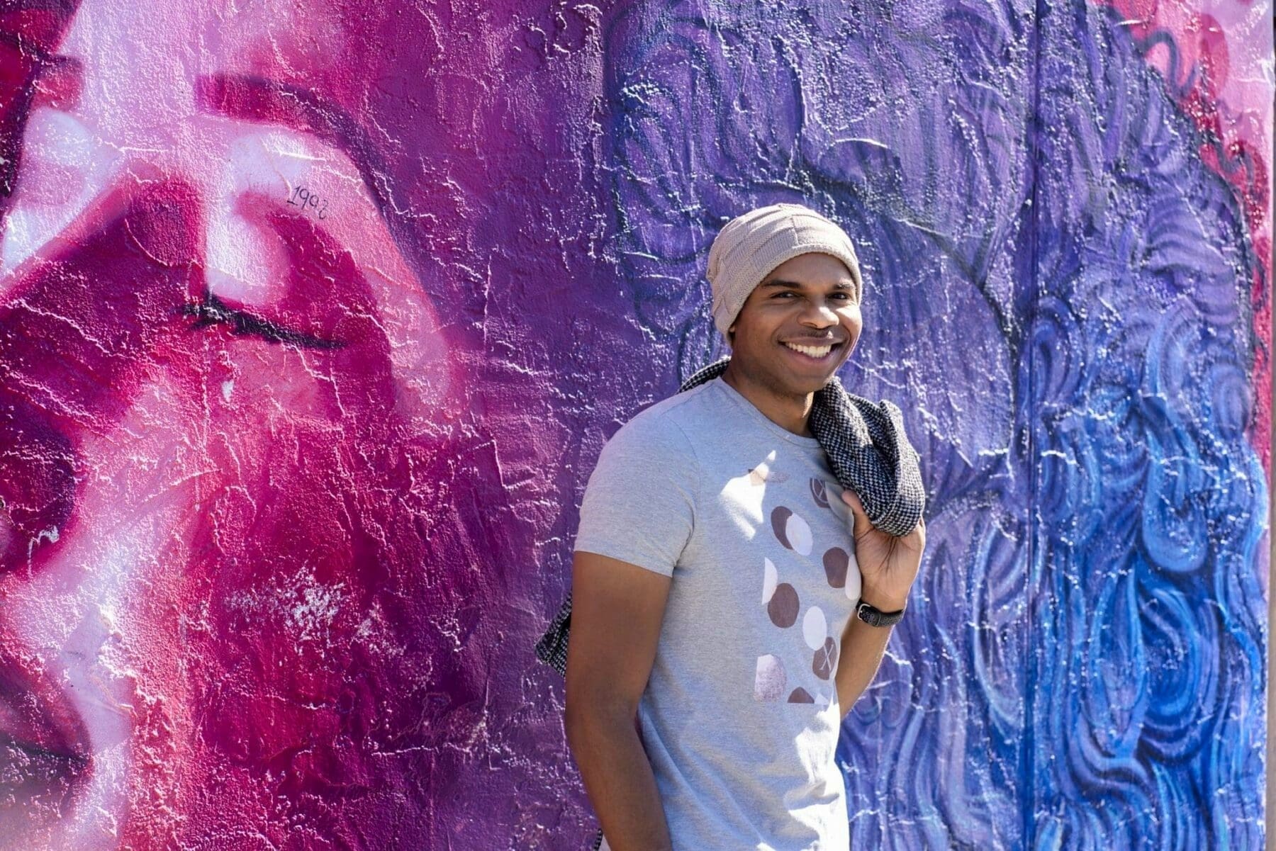 Aaron Owens smiles toward the camera in front of a vivid magenta-and-blue mural.