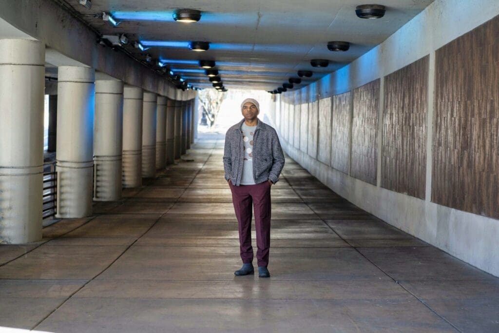 Aaron Owens stands alone at the center of a long covered passage illuminated by blue overhead lights.