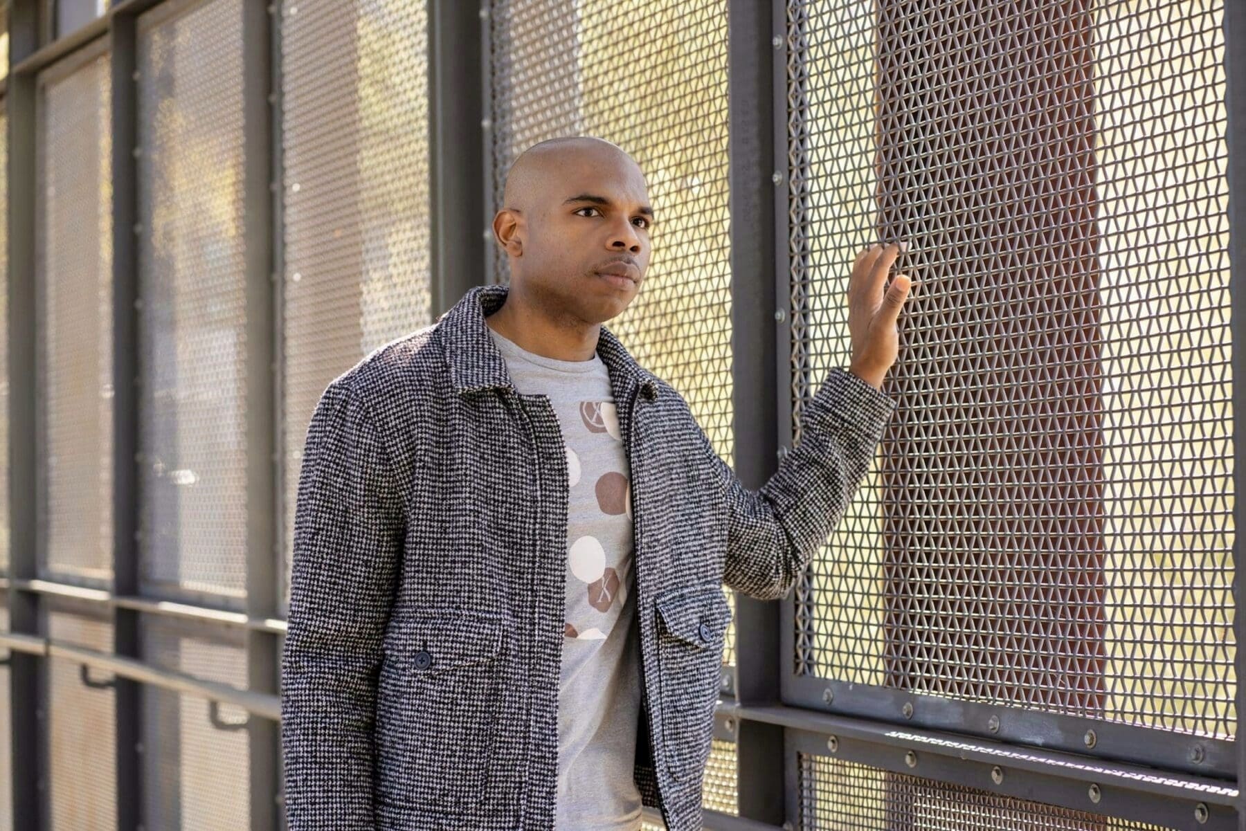 Aaron Owens faces the camera beside a perforated metal screen with warm light filtering through it.