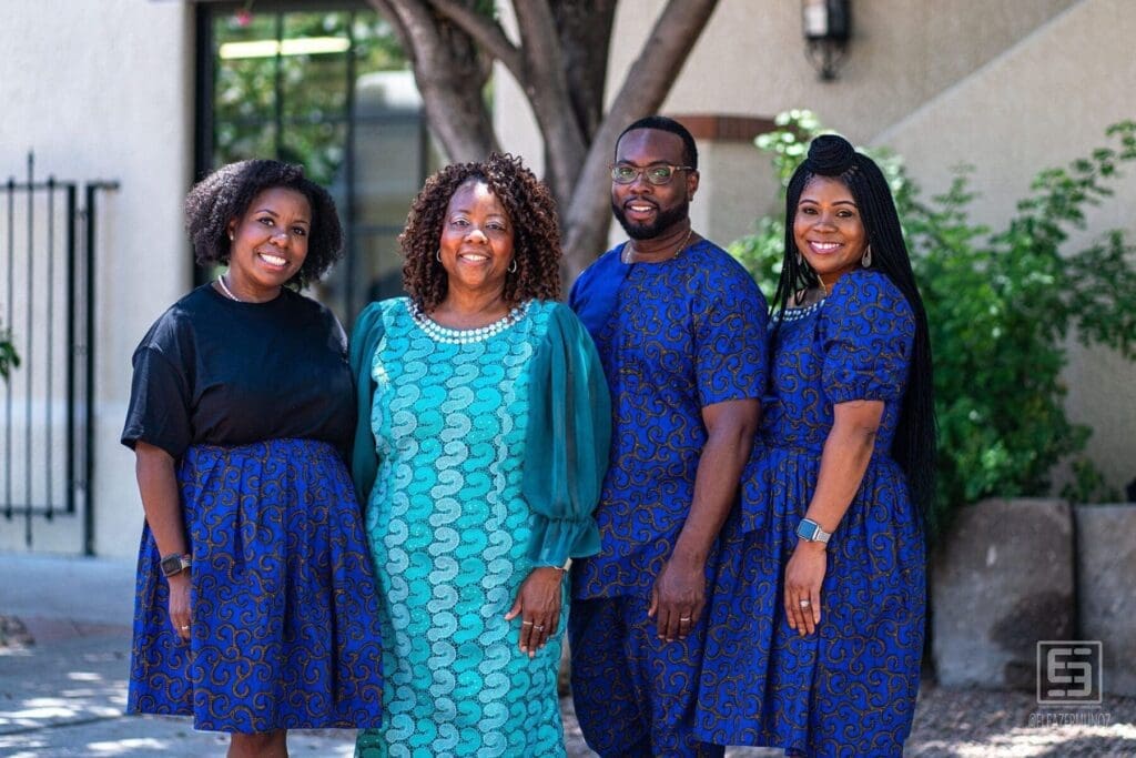 Four adults pose together beneath a courtyard tree in coordinated blue and teal clothing.