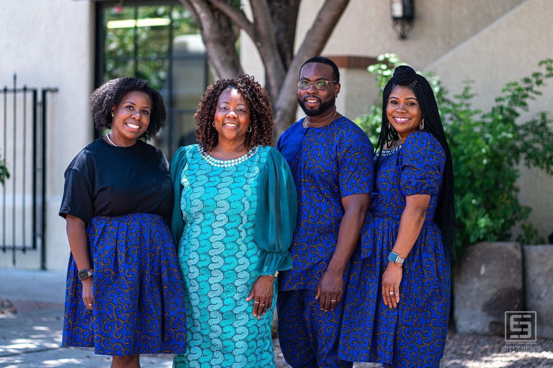 Four adults pose together beneath a courtyard tree in coordinated blue and teal clothing.