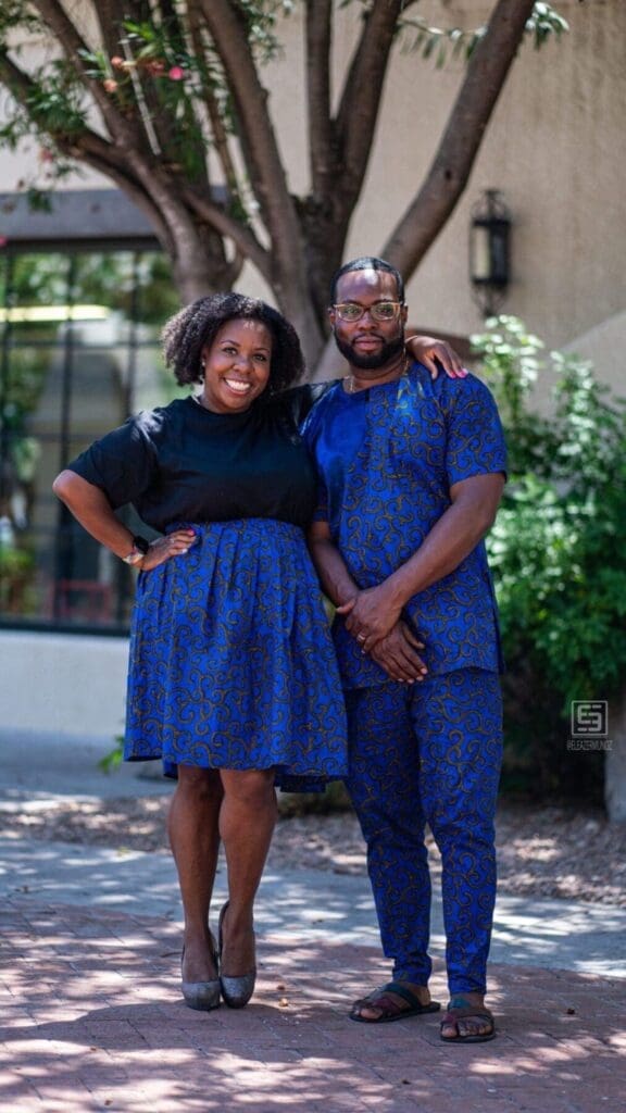 Two adults stand together in a vertical portrait beneath a courtyard tree.