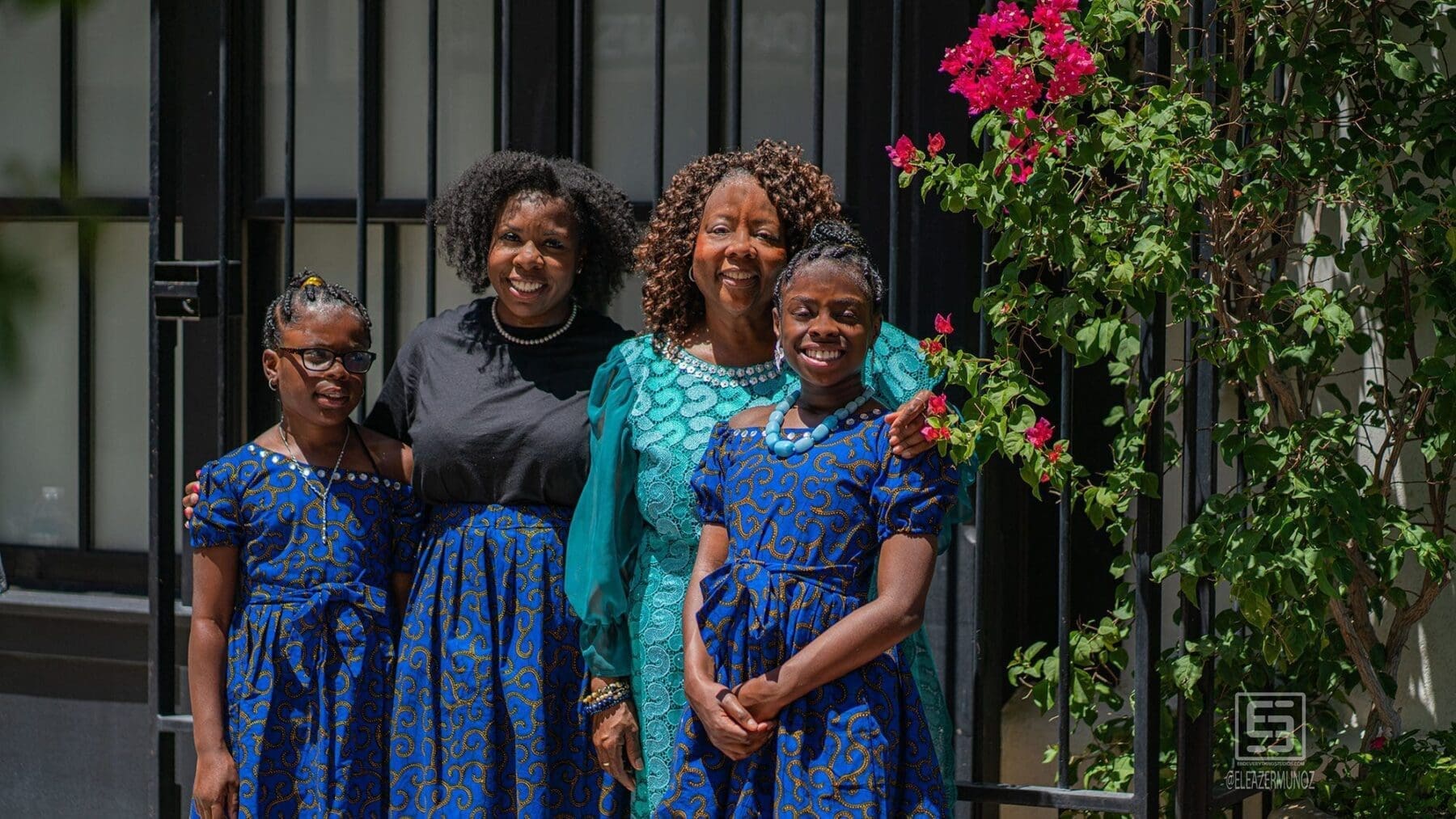 Four women pose together beside a dark doorway and pink bougainvillea.