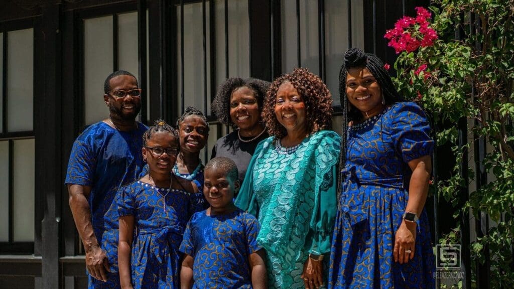 The full family group poses together beside a dark doorway and vivid pink bougainvillea.