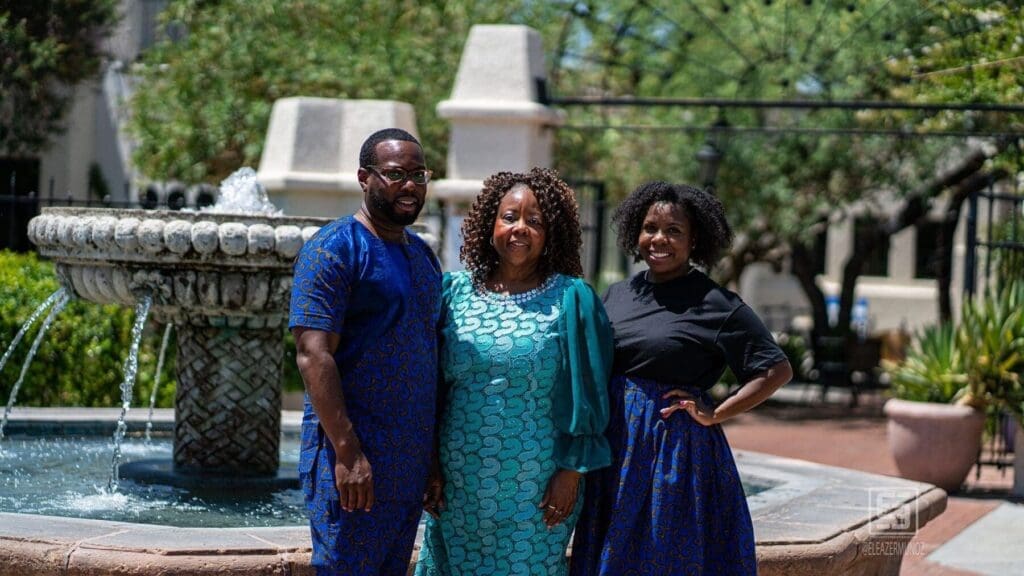 Three adults pose together beside a stone fountain in coordinated blue and teal clothing.